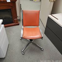 Front view of vintage orange office chair with metal base and casters on carpeted floor.