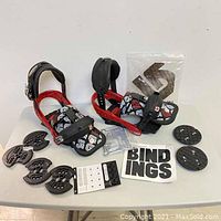 Two red and black Burton snowboard bindings displayed with patterned foot straps, highbacks, mounting discs, and hardware on a white surface