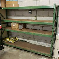 Front view showing four shelves with wood slats in green metal frame against concrete block wall with electrical outlet behind.