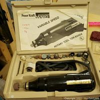 Rotary tool kit inside beige molded plastic case with multiple grinding and polishing bits and original instruction manual in the lid.