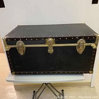 Front view of the Seward storage trunk showing black exterior, brass-tone locks, and reinforced corners.