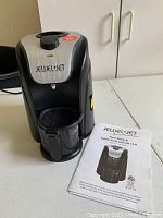 Photo of black and silver Jewel Jet steam cleaning machine and instruction booklet on a white surface.