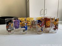 Eight vintage McDonald's collectible drinking glasses arranged in a semi-circle with colorful character designs from the 1970s.
