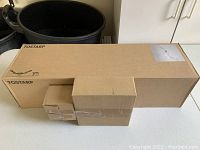 Photo showing four unopened cardboard boxes of IKEA TOSTARP light fixture components, including main fixture and light bulbs, all sealed and new.