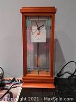 Front view of the Bulova Frank Lloyd Wright clock showing the wooden frame, glass front, clock face, and pendulum.
