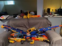 Various Nerf brand foam dart guns and laser tag set piled on a gray covered couch showing color details, types, and quantities.