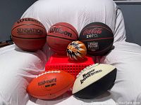 Photo shows 3 basketballs (Wilson Sensation, Wilson, Coca-Cola Zero Final Four), 1 small orange and black bouncy ball, 1 orange glow-in-the-dark football, and 1 black and white football.