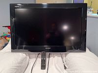 Front view of Sharp Aquos LCD TV with black frame, remote, and power cord shown in front.