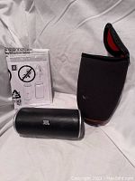 Photo showing the JBL portable speaker, carrying case, and instruction manual on a white background.