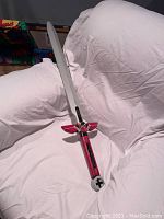 Nerf toy sword laid on a white surface showing entire sword with gray blade and red handle with wing-shaped cross-guard.