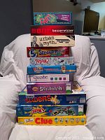 Stack of boxed board games with visible titles including FART!, Bezzerwizzer Urban Myth, Second Rule, PitchPoker, Guess Who?, Equate, Scribblish, Sorry! Sliders, Sorry! Spin, and Clue.