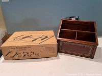 Wooden remote control caddy with three compartments and decorative inlay on front panel next to the unopened desk organizer box.