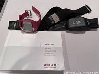 Photo shows Polar FT60 wrist heart rate monitor watch, chest strap sensor, and user manual booklet on a white surface.