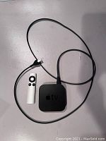 Apple TV device with remote and power cord laid on flat surface.