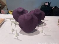 Three purple velvet jewelry display busts on adjustable white stands shown on a table
