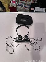 Photo of black Sennheiser on-ear headphones with wired cable and included black zippered carrying case on top of white surface.