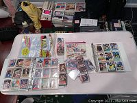 Photo showing assorted vintage baseball and football cards in plastic sleeves, Ziploc bags, and card display sheets on a white table.