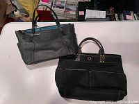Photo showing two leather tote bags on a white surface, one gray Levenger bag and one black Cole Haan bag.
