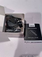 Photo showing the contents of the lot: Jabra Extreme Bluetooth earpiece, charging cable, replacement ear pieces, car charger, and instruction manual.