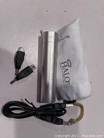 Silver cylindrical Halo Pocket charger alongside black charging cables and white Halo-branded pouch on a gray surface.