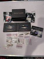 Photo showing 9 boxed Grand Band money and credit card holders, and multiple small plastic bags with extra bands and clasps laid out on a white surface.