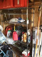 Chrome metal storage rack with wire shelves shown containing various maintenance and cleaning liquids, stored in a garage shed environment.