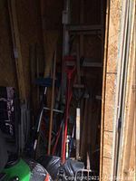 Photo showing arrangement of yard tools including shovels, brooms, and walking sticks leaning in a storage space.