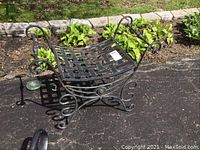 Photo of black curved metal bench outdoors showing lattice seating area and scrolling decorative legs and arms
