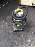 Full view of Stanley wet/dry vacuum showing overall condition, color, and hose coiled on top.