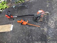 View of Black & Decker electric edger with adjustable depth and electric hedge trimmer on asphalt surface.