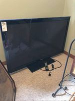 Full view of Samsung TV with stand, remote and power cables on carpeted floor.