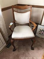 Front view of the carved oak armchair showing carved arms, top rail and cream upholstery
