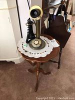 Full view of brass candlestick telephone resting on wood tripod side table