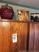 Three McCoy cookie jars atop wooden cupboard: large strawberry jar, bear hugging tree jar, and vintage car jar