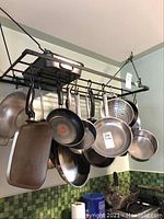 Full view of cooking pots and pans hanging on a rack including frying pans, roasting pan, and strainer.