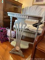 Side view of demi-lune painted wooden table showing spindle legs and curved lower shelf.