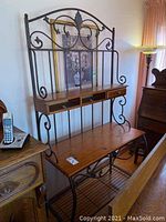 Front view of the metal and wood baker’s rack with decorative swirl metalwork and one wooden drawer present.