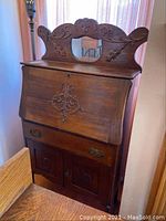 Full front view of oak secretary desk showing carved backboard and drop front closed