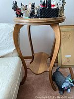 Photo showing wooden elliptical top side table with various ceramic and decorative dog figurines on top, positioned beside a couch and near a small framed item leaning against the wall.