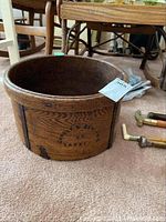 Full view of round wooden cheese barrel showing grain, metal bands, and stamped text.