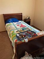 Single wooden sleigh bed fully assembled with colorful Southern Belle appliquéd quilt and assorted jewelry on top of the bed.