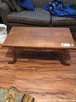 Full view of the rectangular solid oak coffee table in sitting room area with striped couch in background.