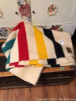 Folded blanket on wooden trunk showing cream field and colored stripes