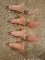 Seven pink tulip-shaped glass lamp shades laid out on beige carpet. Shades show ruffled edges and petal-like flared design with varying pink hues and mottled texture.