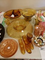 Overview image displaying an assortment of amber and pink pressed glass items including divided servers, decorative figurines shaped like boots and shoes, a glass basket, a lidded box, and various bowls.