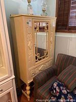 Full view of cabinet with mirrored door, dole on bottom, decorative carvings on sides and front, and turned legs.