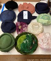 Overall view of collection of eleven vintage women’s hats and one crocheted handbag in peach color