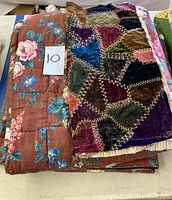 Stack of two vintage quilts, showing a floral patterned quilt on the bottom and a patchwork velvet quilt on top.