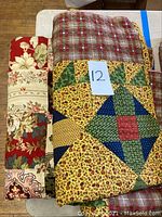 Three vintage quilts folded and stacked, showing patchwork with floral and geometric patterns.