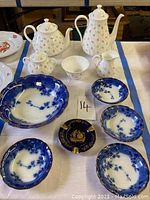 Full set of white teapots, sugar bowl, creamer, bowls, Flow Blue dishes, and Limoges ashtray arranged on table.